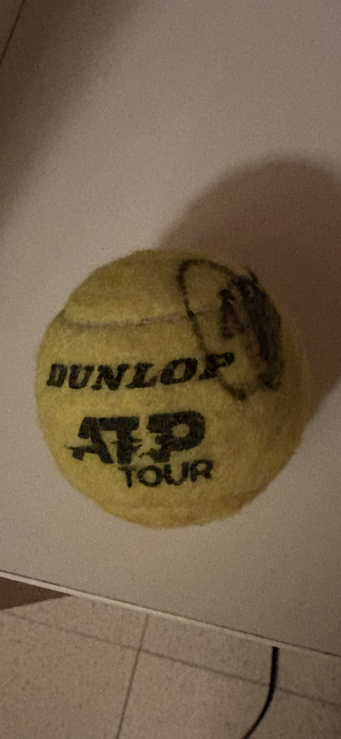 A signed Dunlop ATP Tour tennis ball, resting on a white surface.